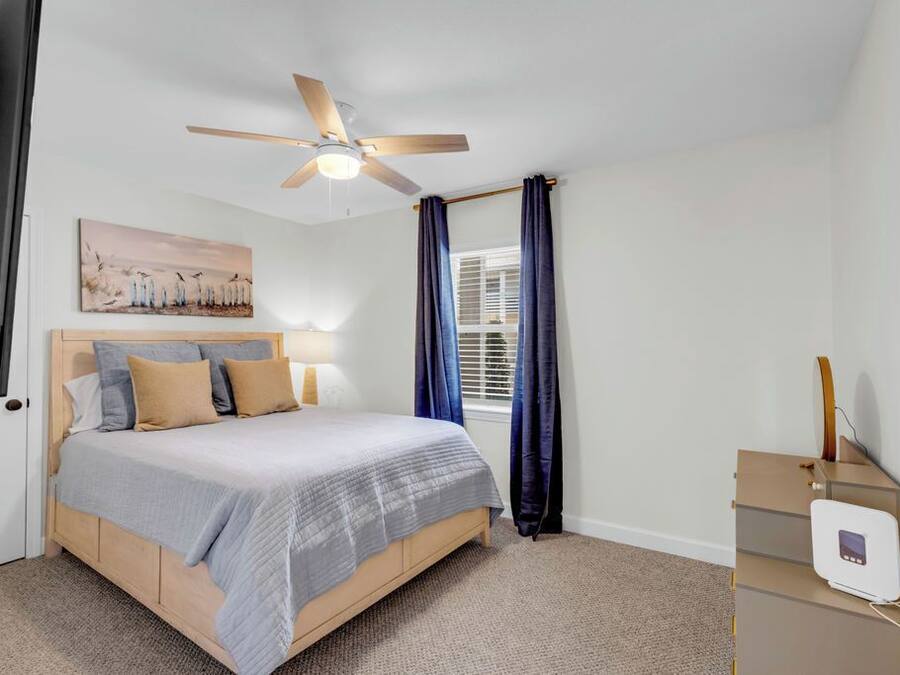A bedroom with a bed, a ceiling fan, a window with curtains, and a bedside table with a lamp.