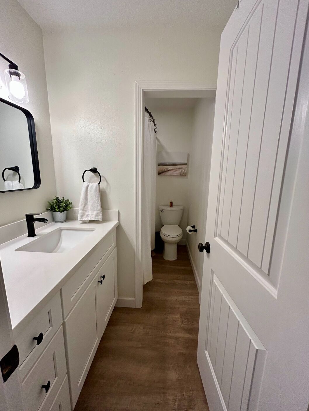 A narrow bathroom with a white sink, a mirror, and a toilet.