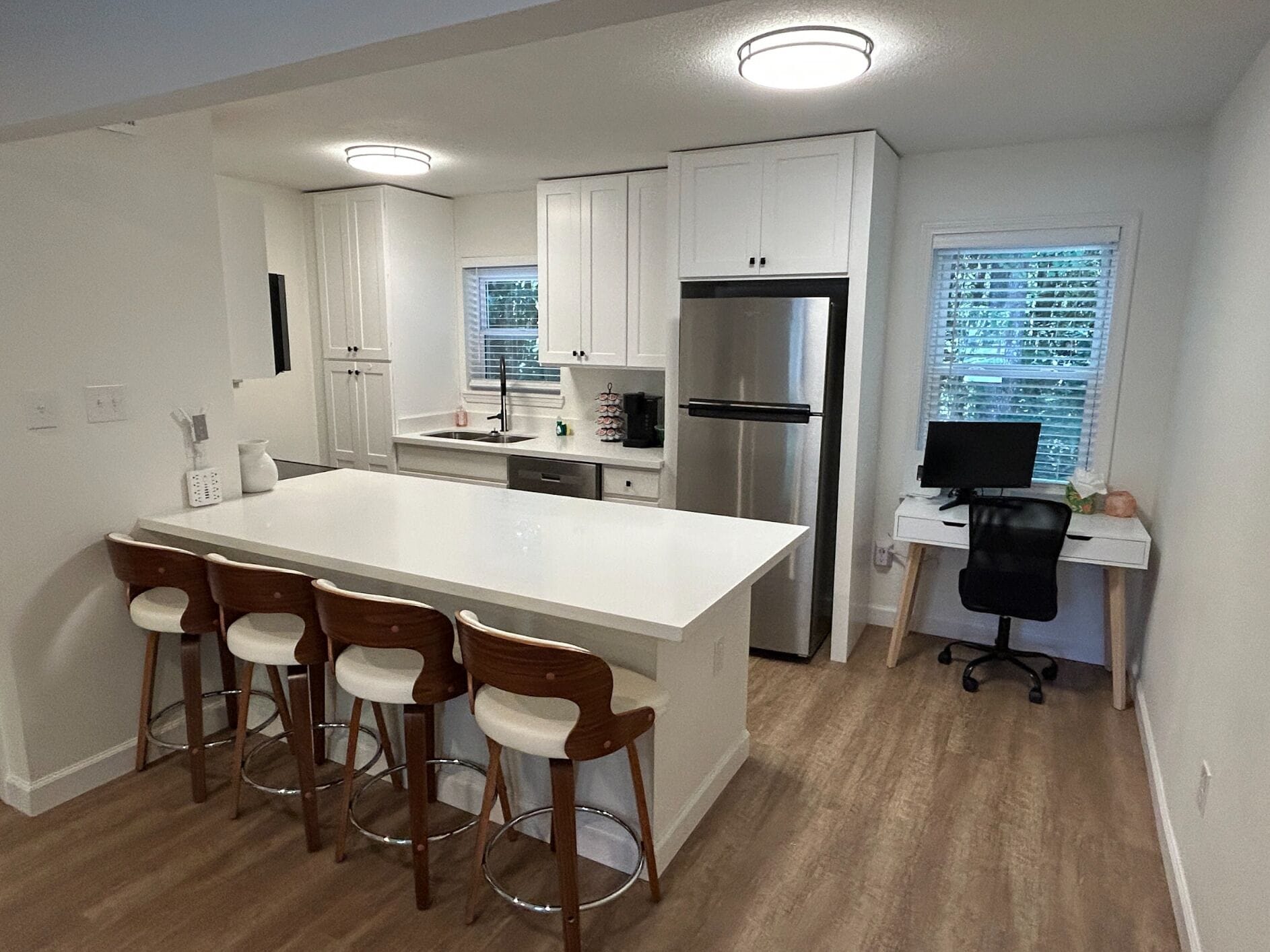 Una cocina moderna con una isla grande, taburetes de bar, un refrigerador y un escritorio para computadora.