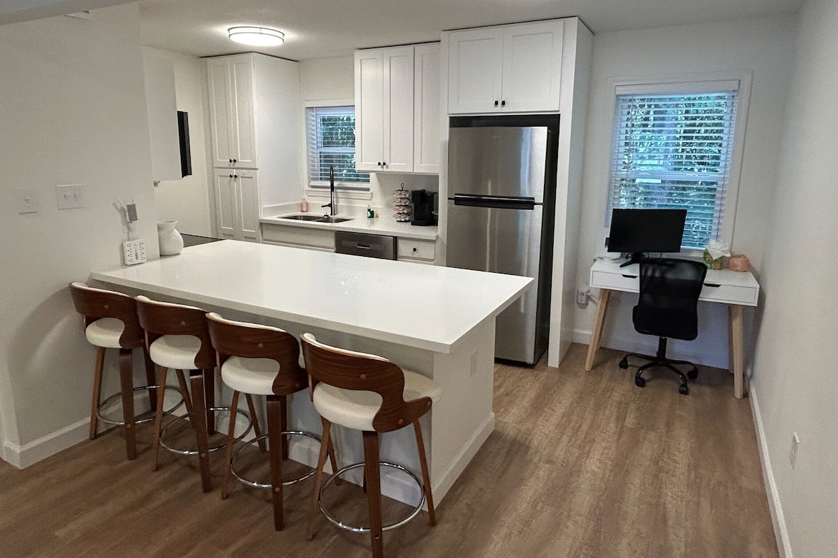 A modern kitchen with a large island, bar stools, a refrigerator, and a computer desk.