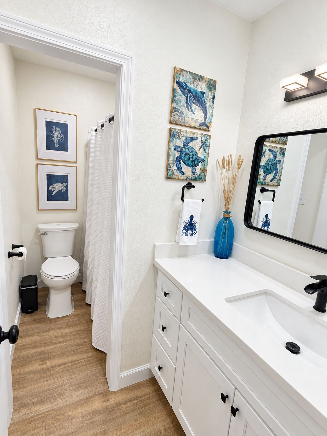 A bathroom with a white toilet, a sink with a mirror, and framed artwork on the wall.