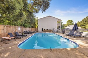 Una piscina rectangular con borde de azulejos, rodeada de sillas de descanso y una valla de madera.