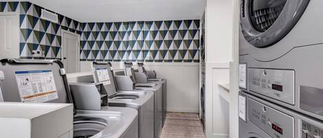 A laundry room with multiple washing machines and dryers, a patterned wall, and a carpeted floor.
