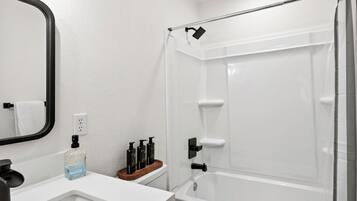 Un baño con lavamanos blanco, espejo, cortina de ducha y artículos de tocador sobre una bandeja de madera.