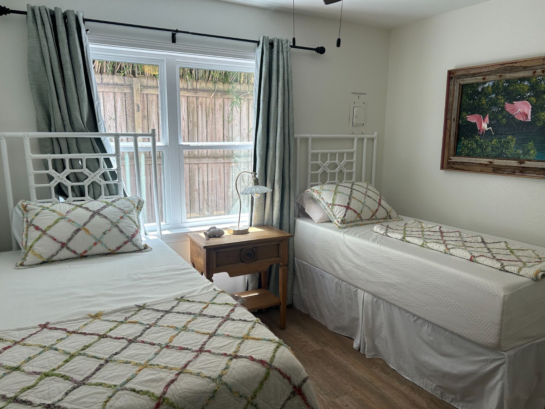 A bedroom with two single beds, a wooden nightstand, a lamp, and a painting on the wall.