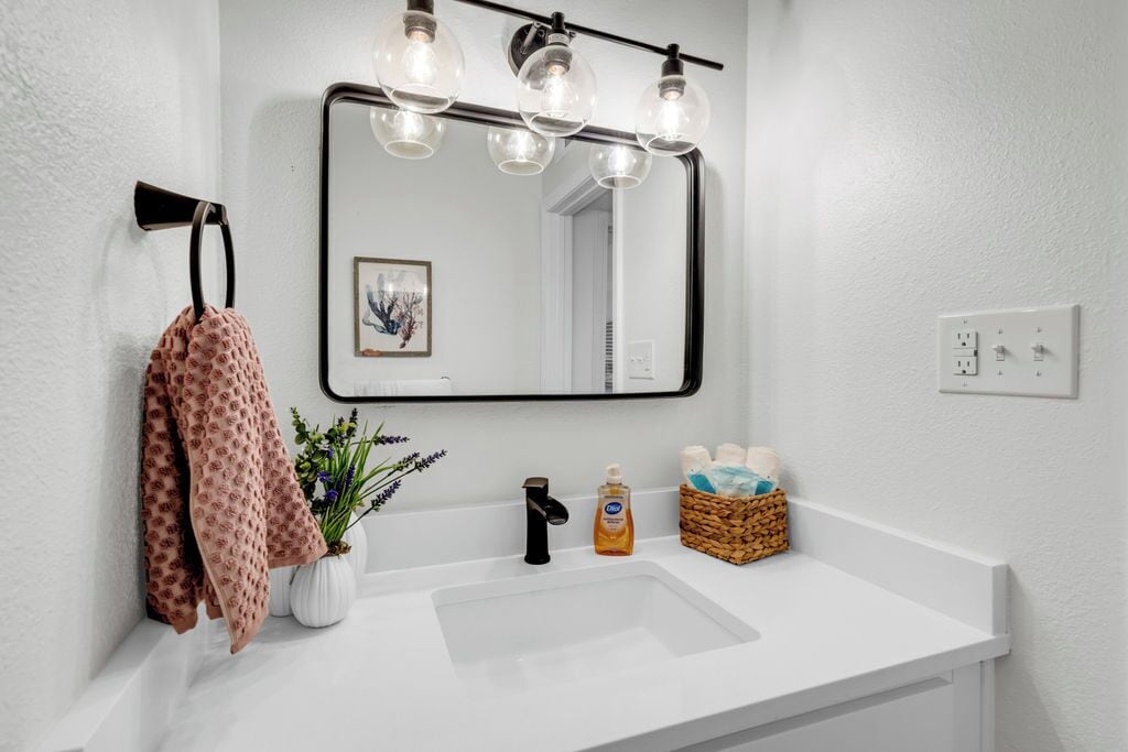 A bathroom with a white sink, black faucet, and a mirror with a light fixture above it.