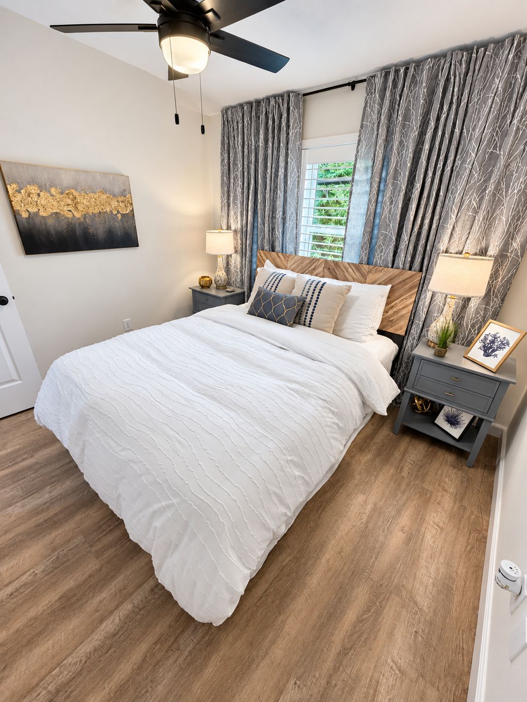 A bedroom with a bed, two bedside tables, a ceiling fan, and a window with curtains.
