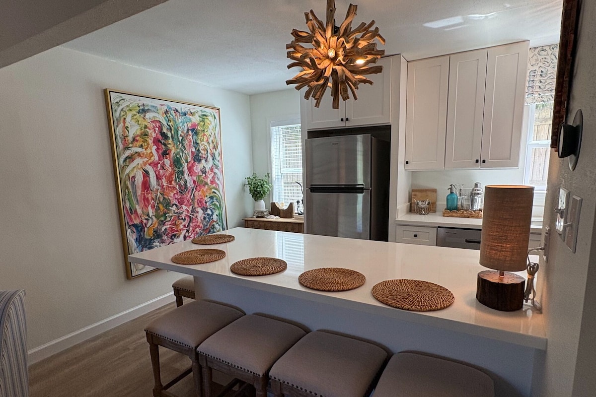 A modern kitchen with a central island, bar stools, a stainless steel refrigerator, and a large abstract painting on the wall.