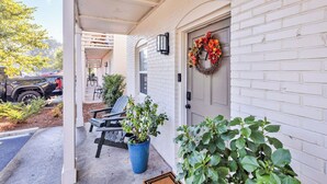 A covered porch with a white brick wall, a door with a wreath, and a blue potted plant. - Porter Condos (Ocean Springs)