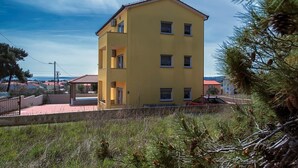 A yellow multi-story building with a balcony, surrounded by greenery and a clear sky. - Apartments Robert (73676-A1) - Medulin (Medulin)