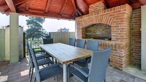 An outdoor patio with a brick oven, a wooden table, and wicker chairs. - Apartments Robert (73676-A1) - Medulin (Medulin)