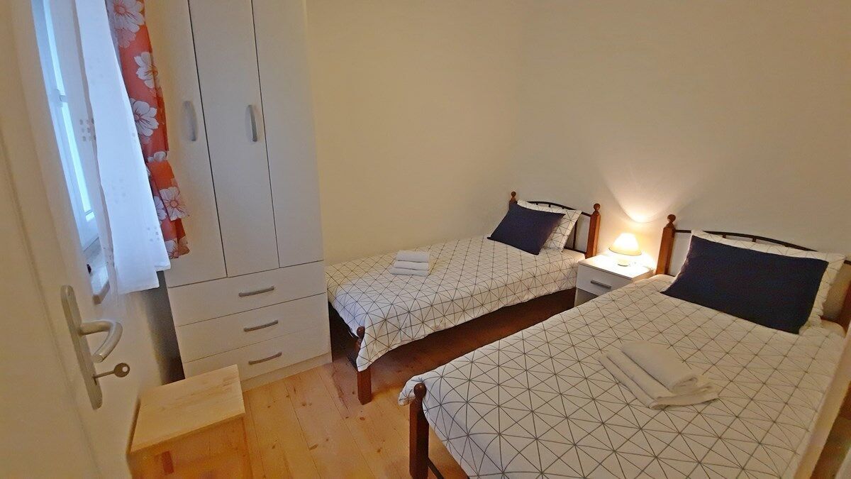 A bedroom with two beds, a wardrobe, and a bedside table with a lamp.