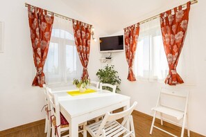 Ein Essbereich mit einem weißen Tisch, Stühlen und einem an der Wand befestigten Fernseher.