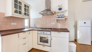 Eine kleine Küche mit weißen Schränken, einem eingebauten Ofen, einer Edelstahl-Dunstabzugshaube und einem weißen Kühlschrank.