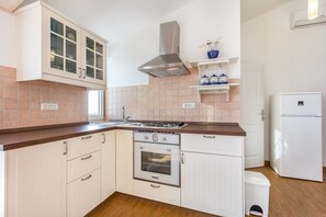 Eine kleine Küche mit weißen Schränken, einem eingebauten Ofen, einer Edelstahl-Dunstabzugshaube und einem weißen Kühlschrank.