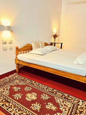 Ein ordentlich gemachtes Bett mit weißen Leinen, einem hölzernen Kopfteil und einem roten Teppich mit Muster.