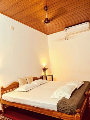 Ein Schlafzimmer mit einem hölzernen Bett, einem Deckenventilator, einer Klimaanlage und einem Nachttisch mit Lampe und Blumen.