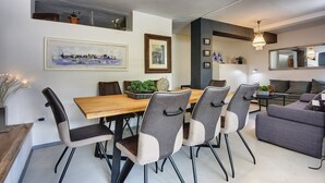 Een moderne eetruimte met een houten tafel en zes stoelen, een schilderij aan de muur en een bank op de achtergrond.