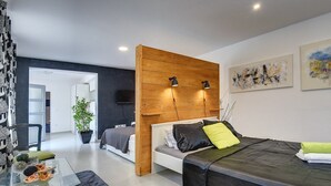 Een moderne slaapkamer met een houten hoofdbord, een glazen bijzettafeltje en een bed met een zwarte matras en groene kussens.