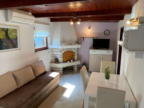 A cozy living area with a stone fireplace, a sofa, a dining table, and a television. - House Dorina (73784-K1) - Pula (Pula)