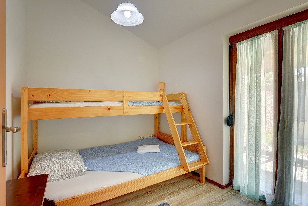 A bunk bed with a ladder, a small desk, and a window with curtains.