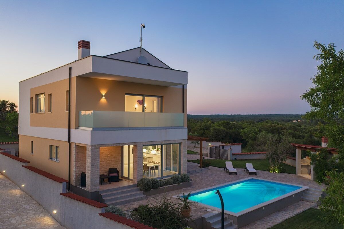 A modern two-story house with a swimming pool, outdoor seating, and a view of the landscape.