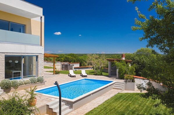Ein modernes, zweistöckiges Haus mit Pool, Außenbereich und Blick auf die Landschaft.