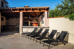 An outdoor patio with lounge chairs, a barbecue area, and a stone wall. - House Fasana (73836-K1) - Fazana (Fazana)
