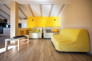 Ein modernes Wohnzimmer mit einem gelben Sofa, zwei Sesseln, einem weißen Couchtisch und einer Küche im Hintergrund.