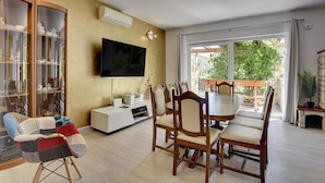 Una sala de estar con una mesa de comedor, sillas, un televisor y un aparador de vidrio.