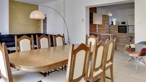 Un comedor con mesa y sillas de madera, un sofá y una cocina al fondo.