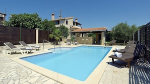 Una piscina rectangular con borde de azulejos, rodeada de sillones de descanso y una terraza con losetas de piedra.