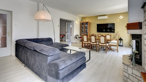 Una sala moderna con un sofá seccional gris, una mesa de centro, una zona de comedor con sillas de madera y un televisor montado en la pared.