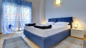 Camera da letto con un letto grande, un comodino, una lampada a parete e una finestra con tende a motivi.