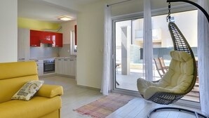 Un soggiorno moderno con un divano giallo, una poltrona sospesa e una cucina con mobili rossi.