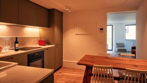 A modern kitchen with a wooden dining table and chairs, a red toaster, and a wine bottle. - Les Deux Mariettes Maison Rose (Lisbon)