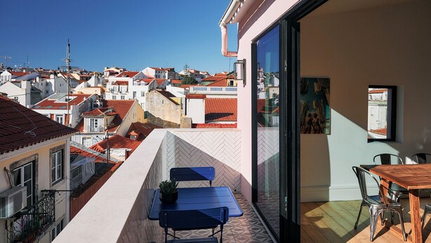 A balcony with a table and chairs, a view of the cityscape, and a painting on the wall. - Les Deux Mariettes Maison Rose (Lisbon)