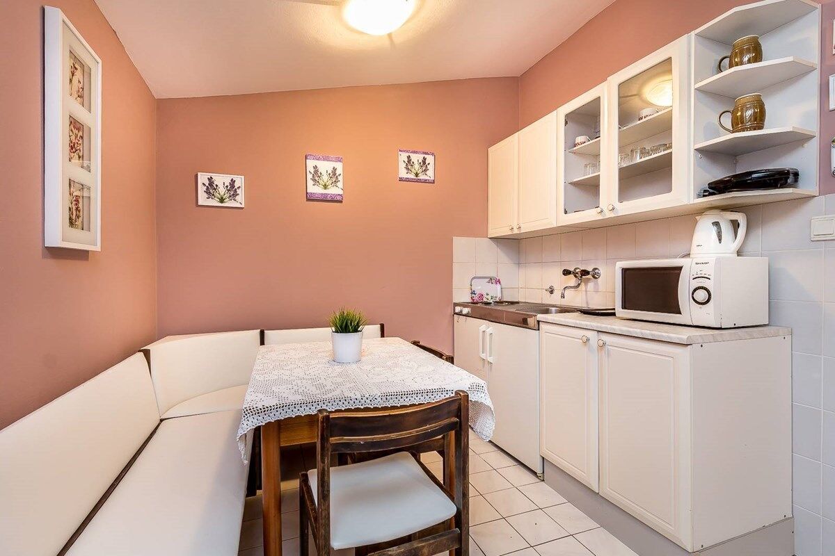 Una cocina compacta con armarios blancos, un microondas y un pequeño comedor con mesa y sillas.