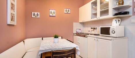 Una cocina compacta con armarios blancos, un microondas y un pequeño comedor con mesa y sillas.