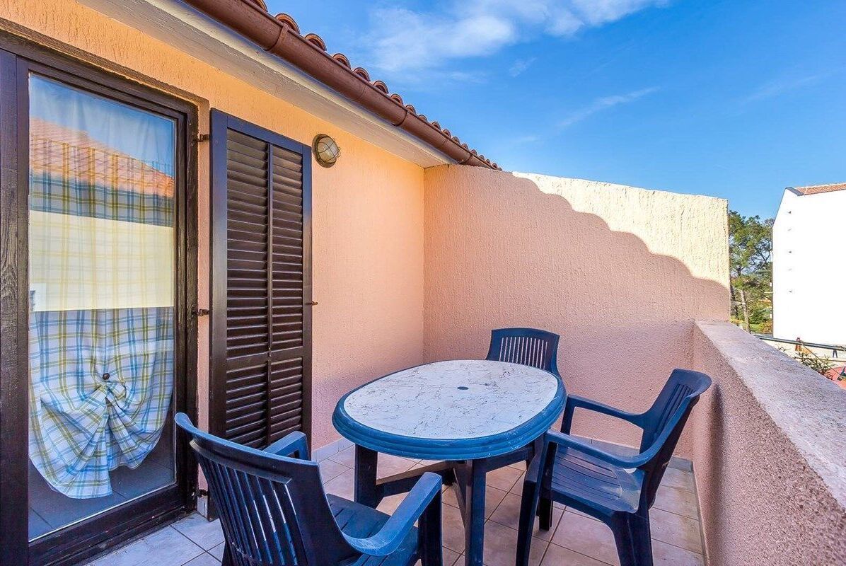 Een balkon met een ronde tafel en vier stoelen, een schuifdeur en een geruit gordijn.