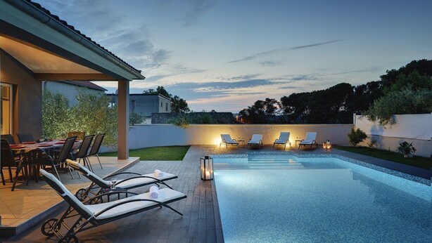 Un espace piscine extérieur moderne, doté de chaises longues et d’un coin repas.