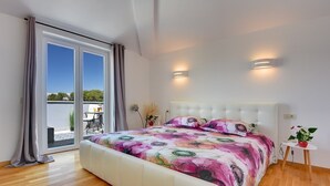 Une chambre dotée d’un grand lit, d’une porte-fenêtre coulissante donnant sur un balcon et de deux lampes fixées au mur.