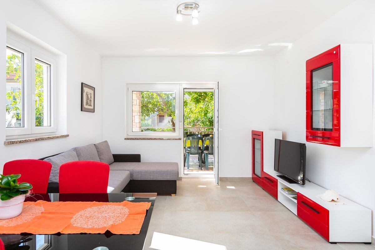 A modern living room with a sofa, red chairs, a dining table, and a TV.