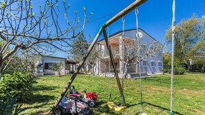Un giardino sul retro con altalena, tosaerba e una casa sullo sfondo.