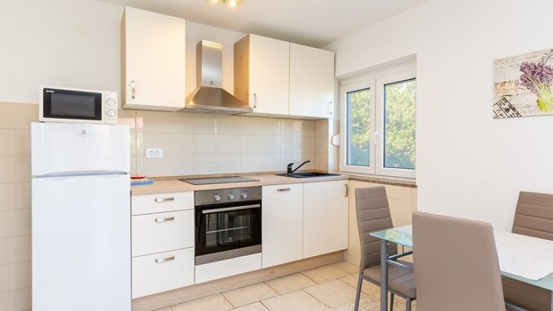 Una cucina moderna con mobili bianchi, forno integrato, microonde e zona pranzo con tavolo e sedie.
