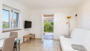 Una stanza moderna con tavolo in vetro, divano, TV e balcone con vista sul verde.