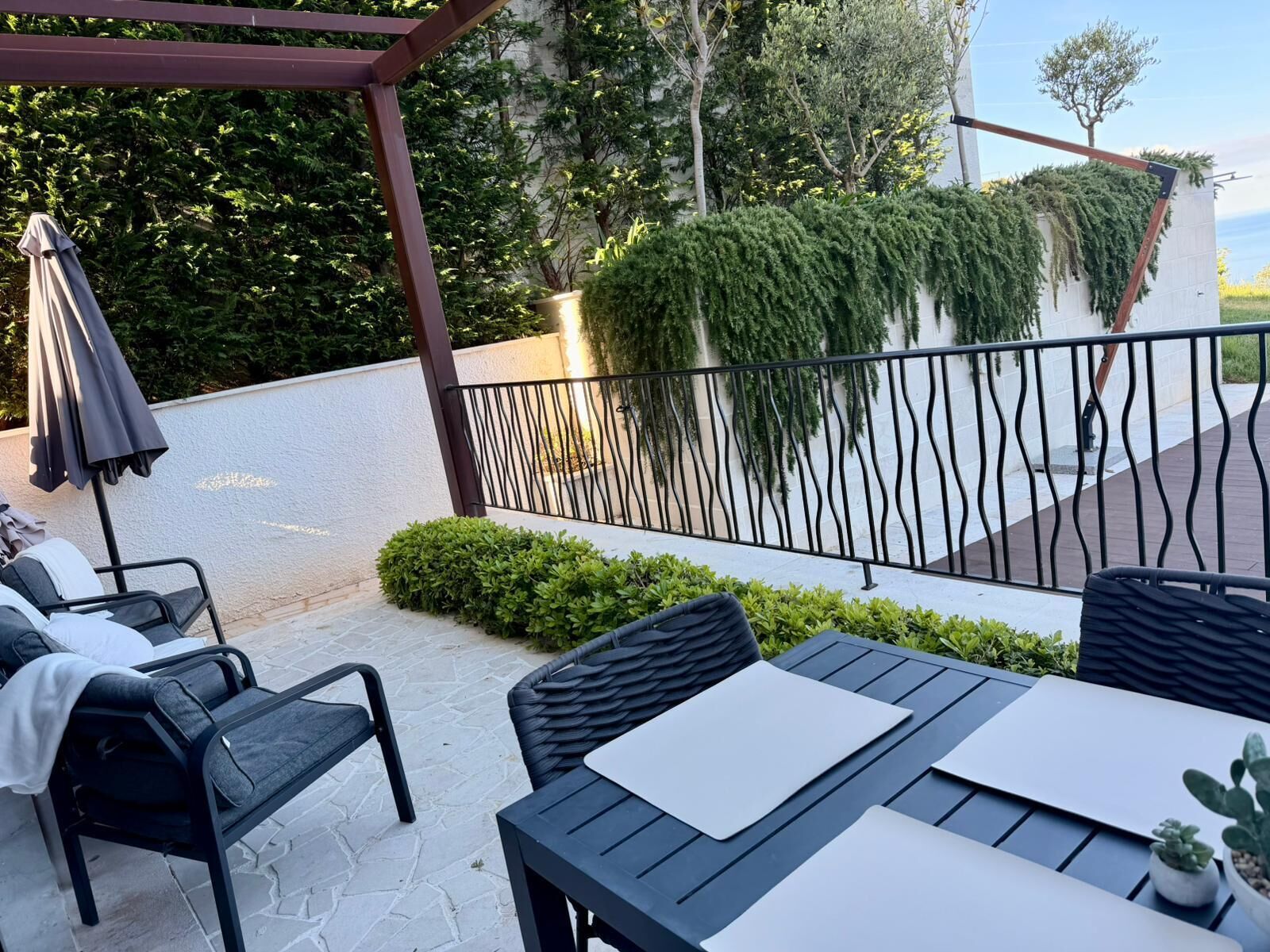 Une terrasse extérieure avec une table et des chaises, une pergola et une rambarde agrémentée de verdure.