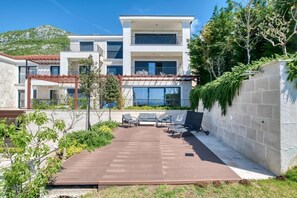 A modern two-story building with a patio area featuring outdoor seating and a pergola. - Seaview Hideaway- Premium Apartment (Sveti Stefan)