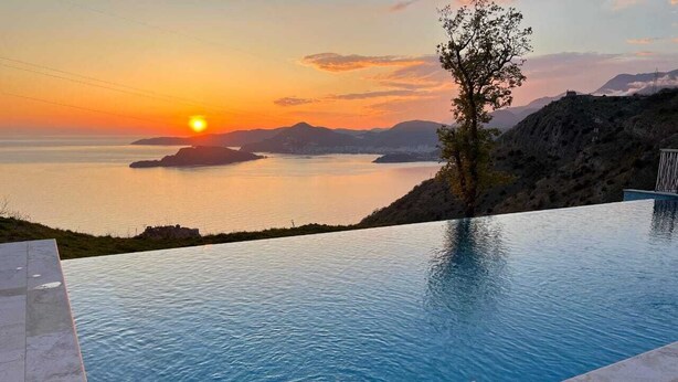 Une piscine avec vue sur le coucher de soleil, un arbre et un paysage rocheux.