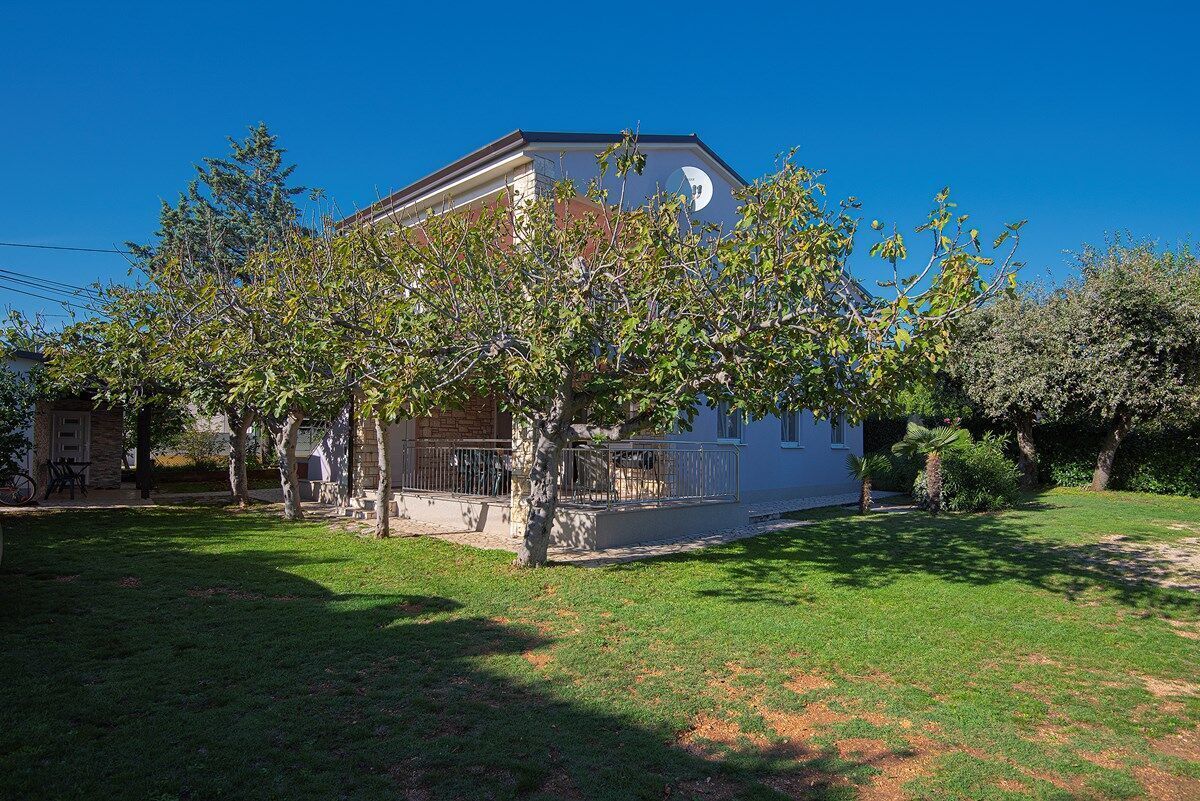 Une maison à deux étages dotée d’un balcon, entourée d’une pelouse bien entretenue et d’arbres.
